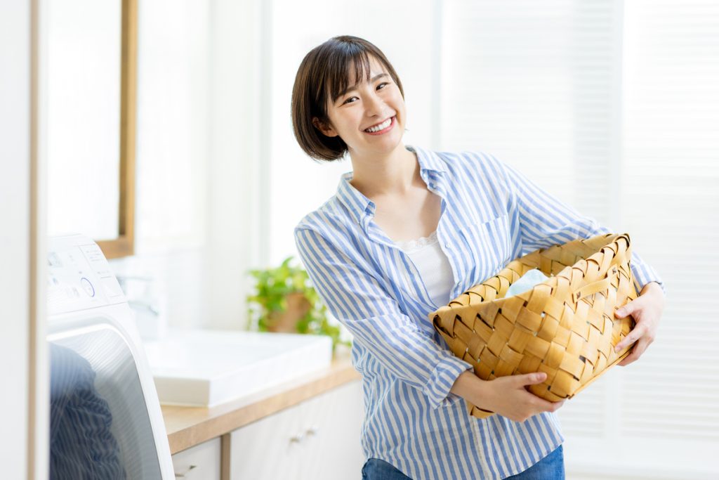 洗濯機の前で洗濯カゴを持つ笑顔の女性