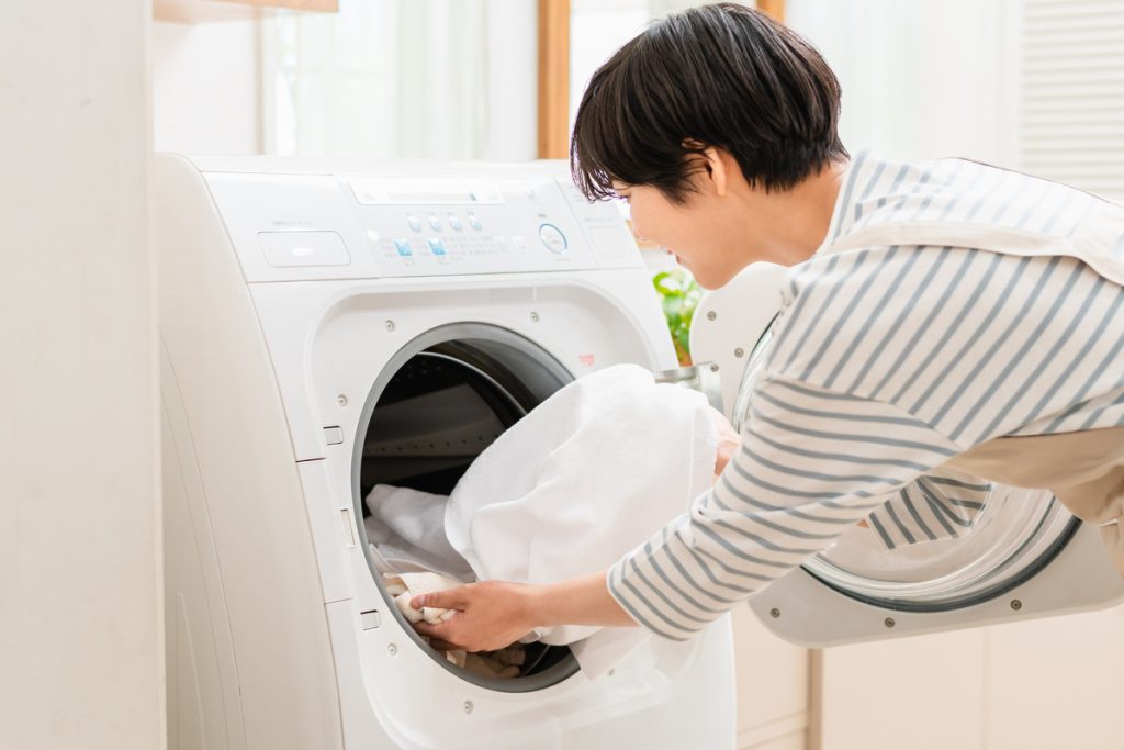 白いシャツを洗濯機に入れる女性